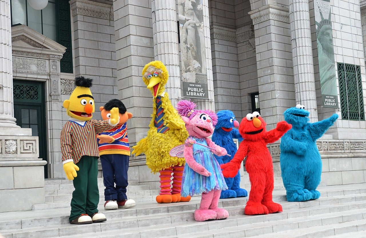 Image of people wearing Sesame Street character costumes standing on steps in front of a building