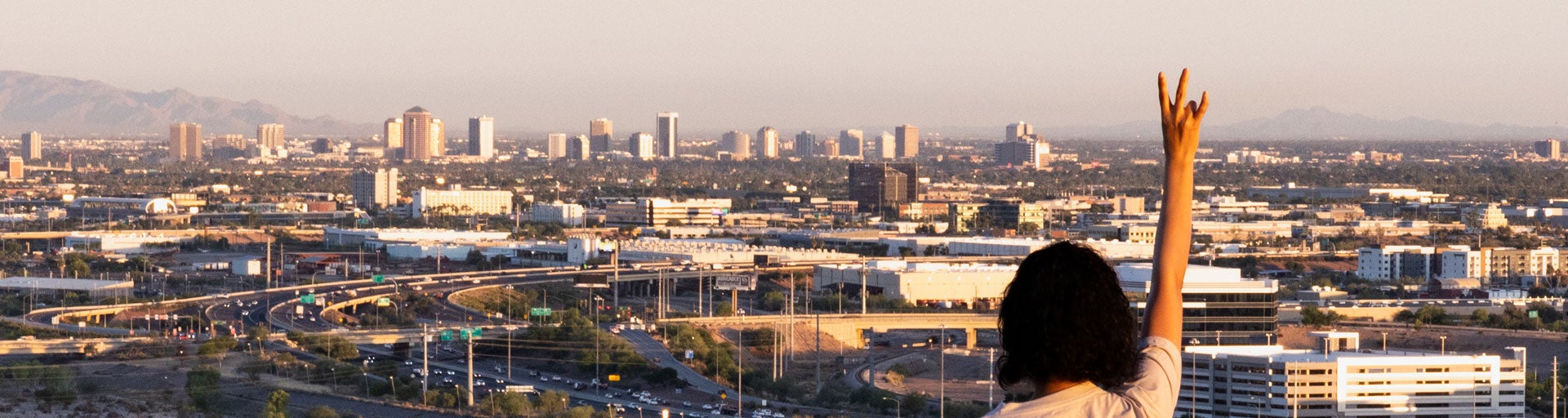 student showing hand sign pitchfork in front of asu phoenix skyline