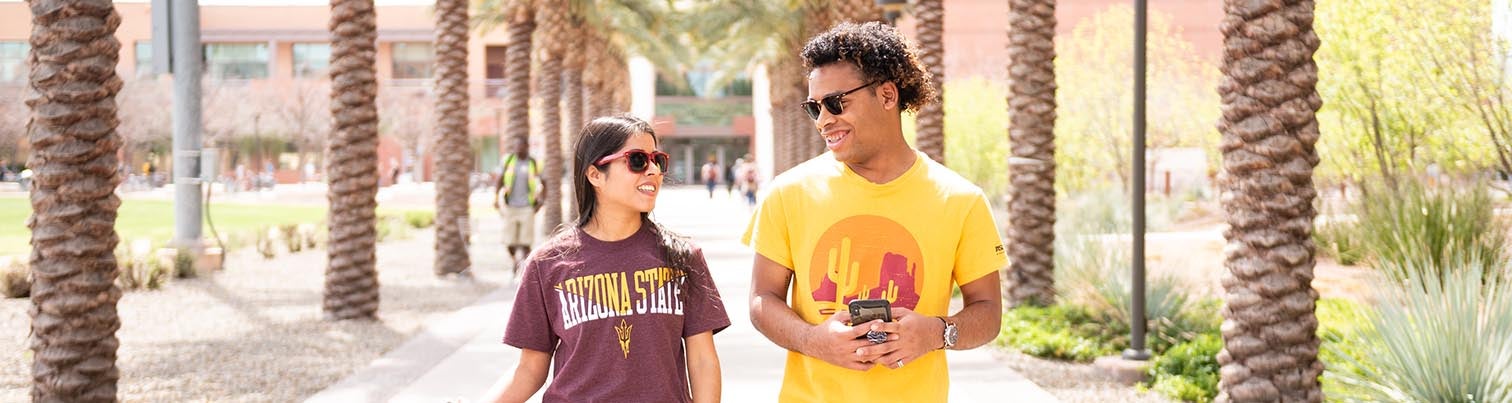 Two students wearing ASU shirts walking down a path framed by palm trees