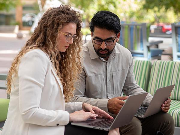 two graduate students reviewing their work on laptops side by side outside