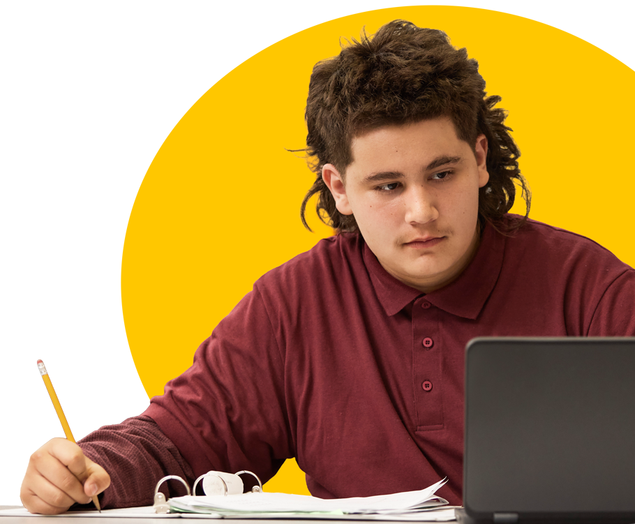 student writing on paper while viewing their laptop