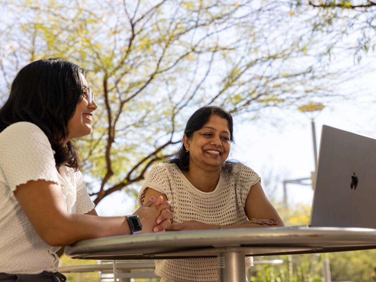 two people sitting at at table outside looking at a laptop screen