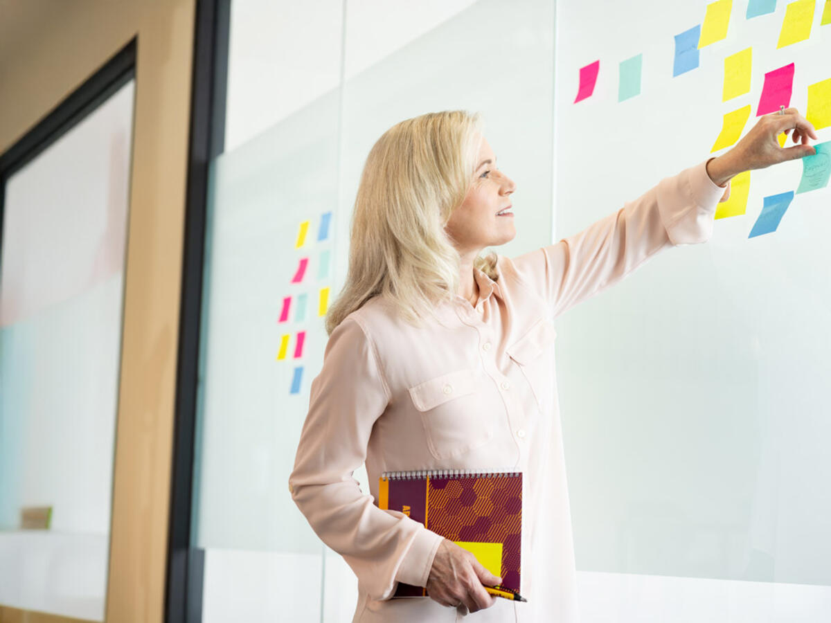 woman arranging multi-colored stickie notes on a whiteboard
